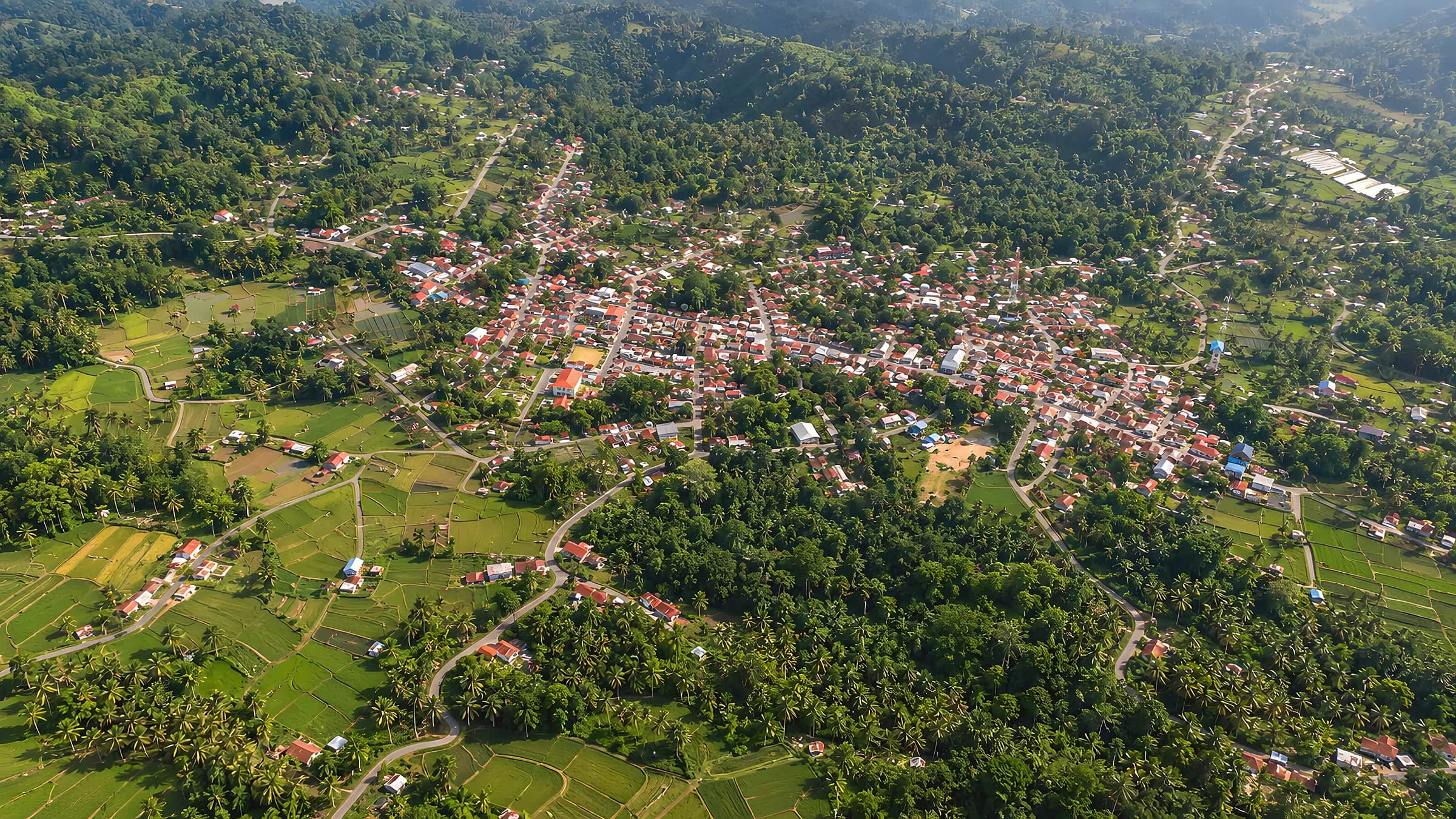 Foto udara Taratara II: permukiman di lembah dikelilingi sawah, kebun kelapa, dan perbukitan